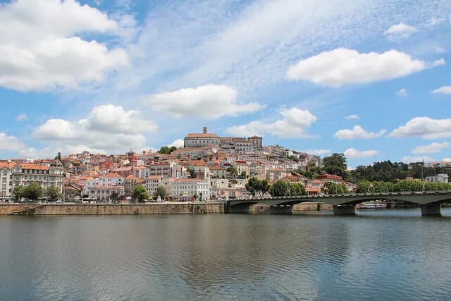 Estudantes trajados com capas negras em frente à Sé Velha de Coimbra durante a Serenata Monumental, sob a luz da lua.