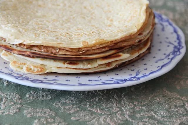 Uma pilha de panquecas caseiras douradas dispostas num prato, polvilhadas com açúcar e canela.