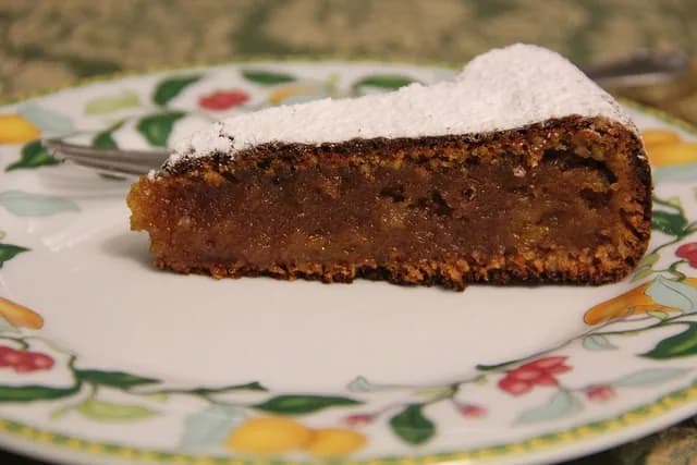 Bolo de dióspiro acabado de cozer, polvilhado com açúcar em pó, servido num prato de cerâmica num ambiente acolhedor.