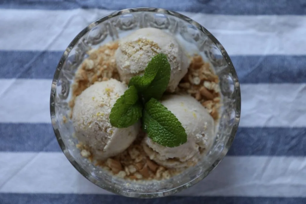 Taça de gelado de banana e laranja polvilhada com bolacha Maria e decorada com hortelã.