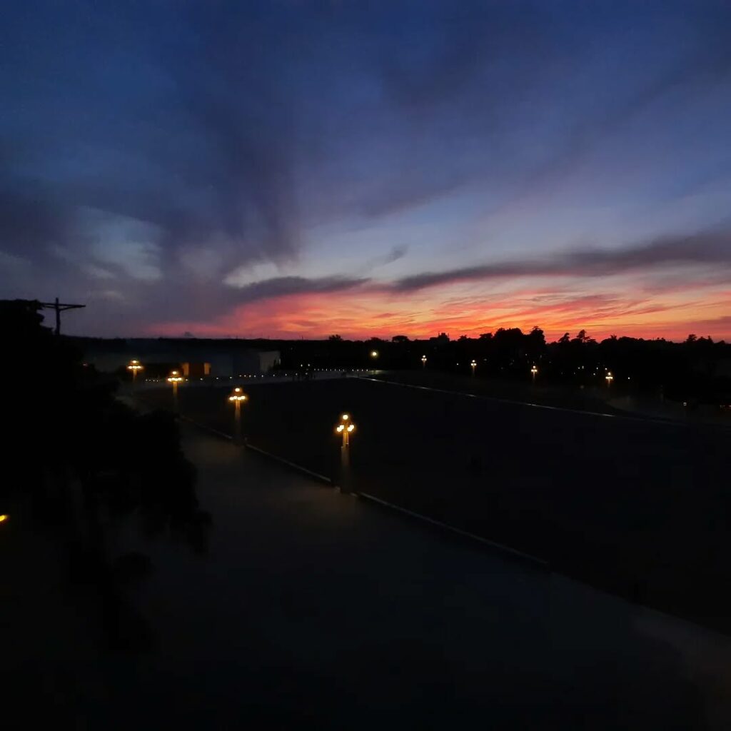 Pôr do sol com céu de tons rosa, roxo e azul escuro sobre a Esplanada do Santuário de Fátima